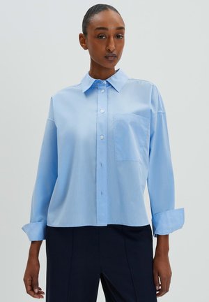 Light blue button-up shirt with a collar, long sleeves, and a chest pocket. Made of smooth fabric, featuring a relaxed fit and cuffed sleeves.
