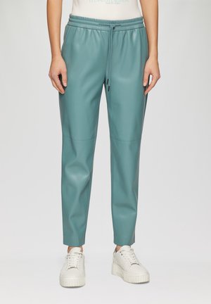 Pantalons en simili cuir teal avec une coupe décontractée, taille à cordon et jambes fuselées. Associés à des baskets blanches à plateforme.