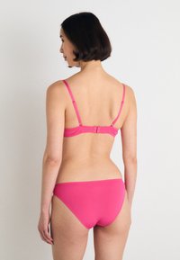 Conjunto de biquíni rosa com alças ajustáveis, fecho de gancho e tecido suave com costuras mínimas. A parte debaixo tem um corte simples e modesto.