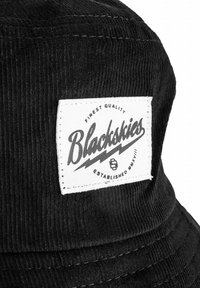 Fekete kordbársony vödrös kalap, amelyen egy fehér téglalap alakú folt található, rajta a "Blackskies" logó fekete szöveggel és díszítő villám akcentusokkal.