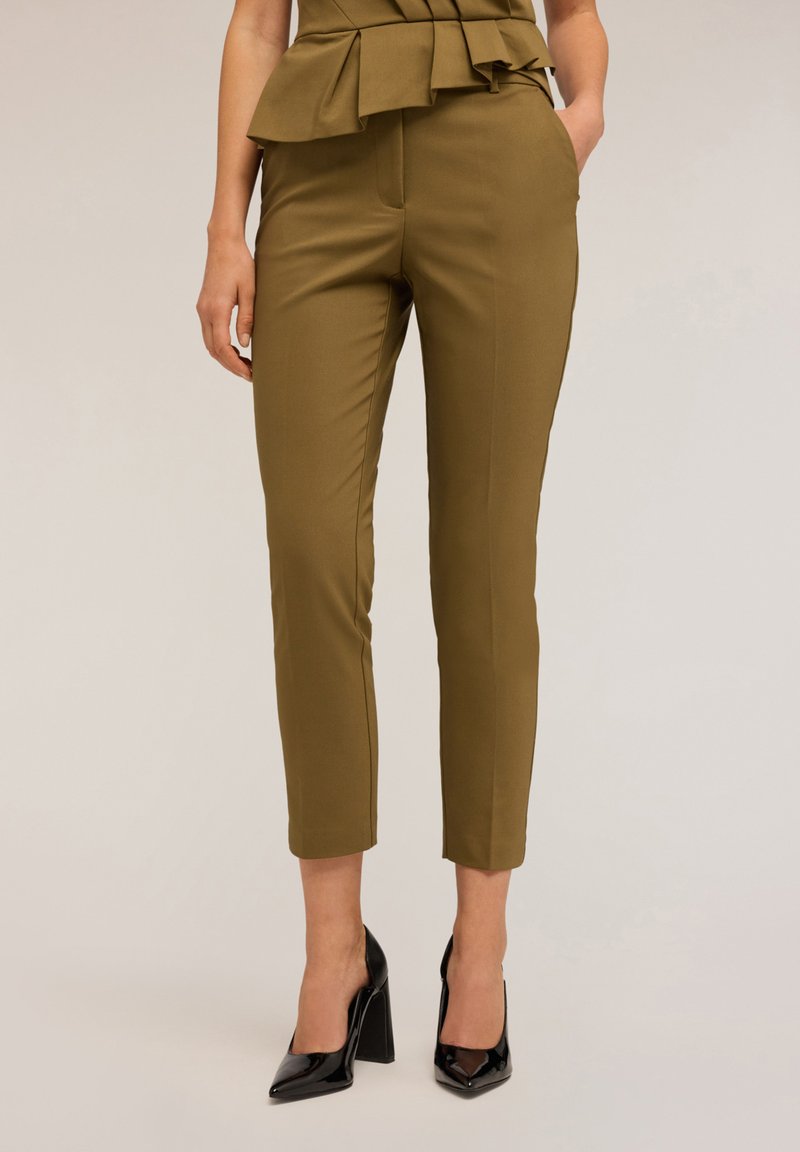 Olivově zelené kalhoty na míru s přiléhavým střihem a bočními kapsami, zdobené peplum akcentem v pase. Černé špičaté podpatky dokončují vzhled.