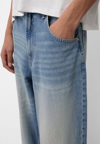 Ljusblå denimjeans med avslappnad passform, synlig blekning, sidofickor och en klassisk midja med dekorativa sömmar.