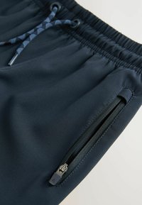 Marineblå atletikshorts lavet af glat stof, med elastisk talje, justerbar snor og lynlåslomme på siden.