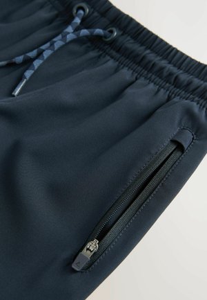 Námornícky modré športové šortky vyrobené z hladkej tkaniny, s elastickým pásom, nastaviteľnou šnúrkou a bočnou vreckou na zips.