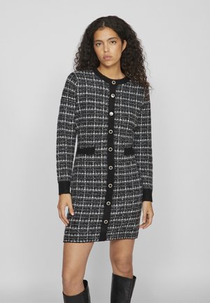 Robe tricotée noire et blanche à carreaux, avec des manches longues, un col rond, des boutons sur le devant et des poches latérales. Tissu texturé, longueur genoux.