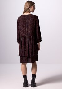 Robe à manches longues de couleur bleu foncé avec un motif abstrait rouge, design en niveaux et détails plissés ; associée à des bottines noires.