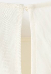 Tela color crema con superficie texturizada, parcialmente abierta, revelando una capa interna. Es visible la costura a lo largo de los bordes, creando líneas limpias.