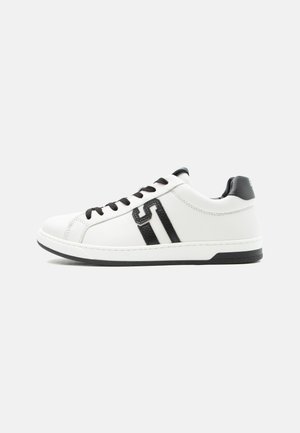 Άσπρο sneaker χαμηλού τύπου με μαύρα κορδόνια, μαύρη ταμπέλα στη φτέρνα και μαύρη λεπτομέρεια λογότυπου "S" στο πλάι, τοποθετημένο σε ανοιχτό φόντο.