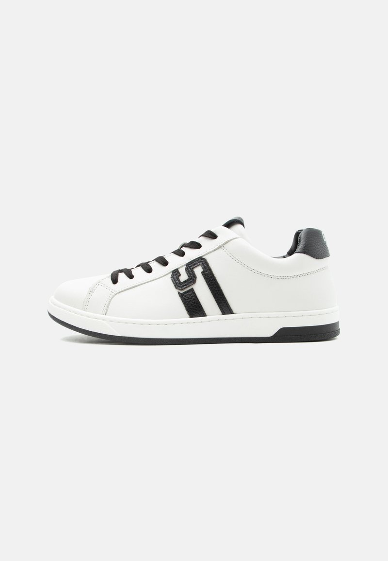 Άσπρο sneaker χαμηλού τύπου με μαύρα κορδόνια, μαύρη ταμπέλα στη φτέρνα και μαύρη λεπτομέρεια λογότυπου "S" στο πλάι, τοποθετημένο σε ανοιχτό φόντο.