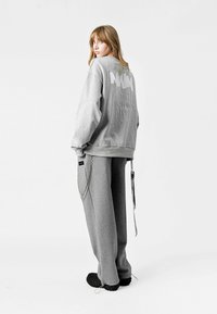 Sudadera gris con cuello redondo y un gran gráfico en la parte posterior, combinada con pantalones de chándal grises que presentan un detalle de cadena lateral. Tejido texturizado.