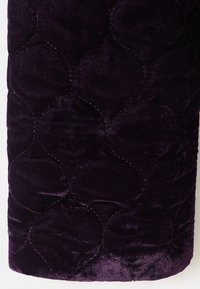Tessuto di velluto viola con un motivo trapuntato di cerchi interconnessi. Texture morbida con linee di cucitura visibili.