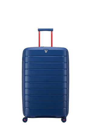 Valigia rigida blu con finitura texturizzata, scanalature verticali, manico telescopico rosso e quattro ruote multicolori per la mobilità.