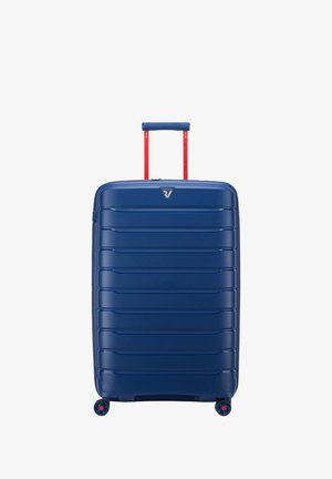 Valigia rigida blu con finitura texturizzata, scanalature verticali, manico telescopico rosso e quattro ruote multicolori per la mobilità.