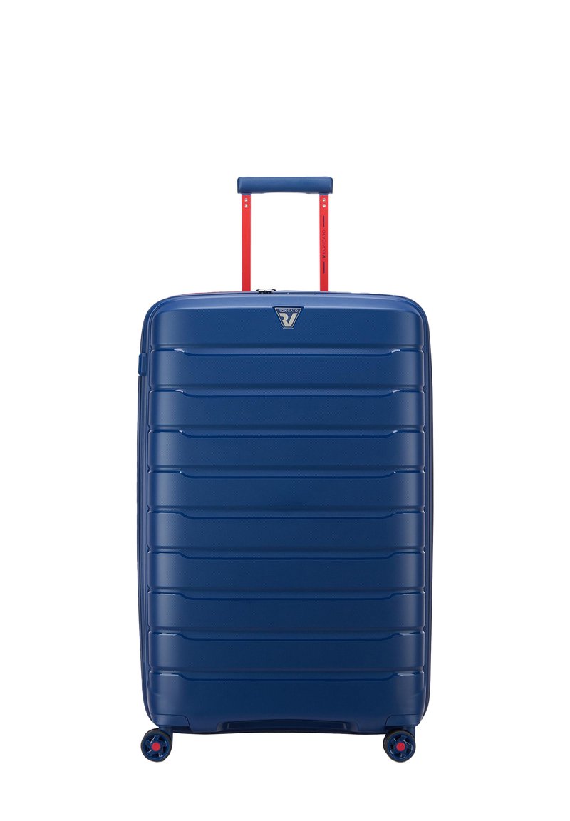 Valigia rigida blu con finitura texturizzata, scanalature verticali, manico telescopico rosso e quattro ruote multicolori per la mobilità.