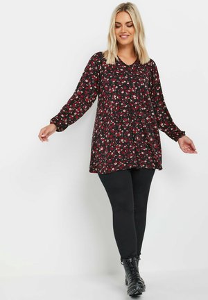 Black floral tunic with long sleeves, featuring a v-neckline and red, white, and green patterns. Paired with black leggings and ankle boots.