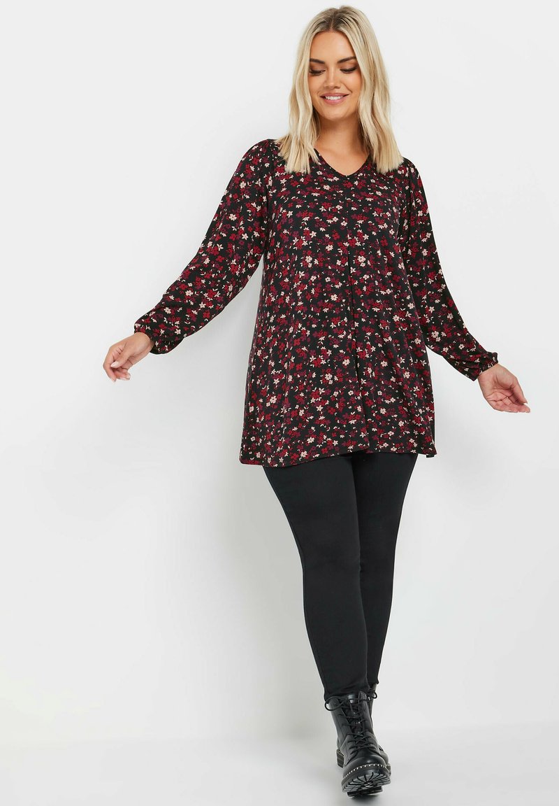 Svart blommig tunika med långa ärmar, med en v-ringning och röda, vita och gröna mönster. Kombinerad med svarta leggings och ankelskor.