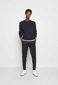 Felpa blu navy con polsini a costine, abbinata a pantaloni della tuta neri a gamba affusolata e sneakers bianche con suola in gomma. Design semplice e minimalista.