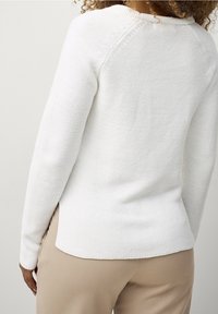 White knit sweater with ribbed texture, long sleeves, and a crew neckline. Side slits at the hem create a relaxed fit.
