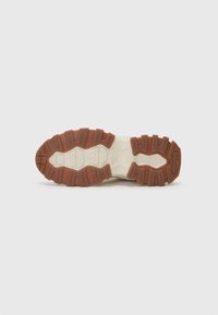 Suola di una scarpa con un design in gomma testurizzata in marrone e crema, con un battistrada pronunciato per presa e stabilità.