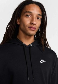 Felpa nera con cappuccio e cordino, logo Nike bianco. Tessuto morbido, vestibilità casual e polsini a coste. Focus sull'area del petto e design del cappuccio.