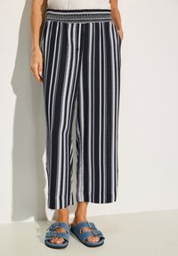 Randiga vida byxor i marinblått och vitt, med elastisk midja och sidofickor. Matchas med blåa slidesandaler med spännen.