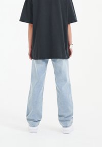 T-shirt nera oversize con una vestibilità rilassata, abbinata a jeans dritti azzurri e sneakers bianche, vista da dietro.