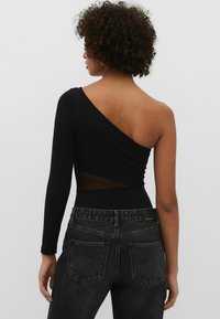 Bodysuit noir à une épaule avec un panneau arrière en mesh, présentant des manches longues et une coupe ajustée, associé à un jean taille haute foncé.
