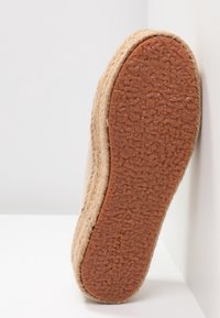 Suola di una scarpa espadrille realizzata in juta naturale con un fondo in gomma marrone texturizzato. Forma rotonda con un bordo intrecciato e finitura liscia.