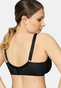 Donna vista di spalle che indossa un reggiseno nero con spalline regolabili e i capelli raccolti in una coda di cavallo bassa.