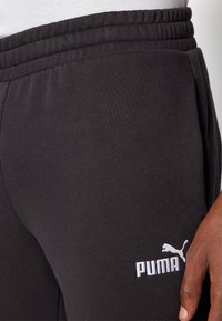 Zwarte joggingbroek van zacht materiaal, met een elastische tailleband en zijzakken. Het Puma-logo is in het wit prominent afgebeeld.