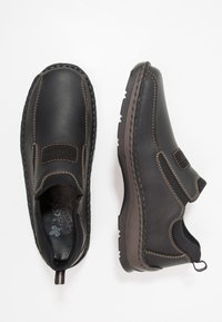 Zwarte leren instapschoenen met een gladde afwerking, bruine stiksels, een elastische paneel en een gestructureerde rubberen zool. Voorzien van een lus aan de achterkant voor eenvoudig aan- en uittrekken.