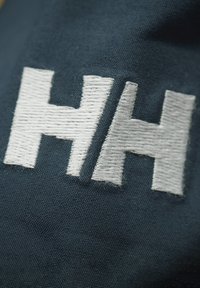 Tessuto blu navy che mette in risalto un logo ricamato prominente in bianco, con le lettere "H" e "H" in uno stile audace e blocco con filo testurizzato.