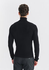 Czarny dopasowany sweter z kołnierzem typu golf z prążkowanej tkaniny i długimi rękawami, z wysokim kołnierzem i gładkim wykończeniem. Prezentacja z tyłu.
