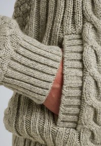 Maglione a treccia in beige chiaro, con polsini a costine e una tasca frontale, che presenta un motivo di maglia testurizzata e spessa.