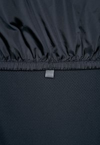 Chaqueta negra con una cintura elástica fruncida. Tejido suave y ligero con una textura sutil. Cuenta con una pequeña lengüeta para ajuste.