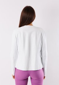 Giacca di pelle bianca con maniche lunghe e collo rotondo. Presenta una vestibilità sagomata e dettagli delle cuciture sul retro. Abbinata a pantaloni viola.