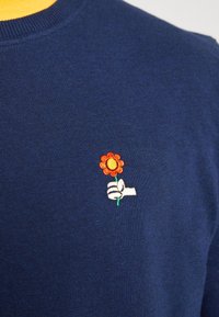 Navy sweater featuring a small embroidered design of a flower held by a hand, with bright orange petals and a yellow center.