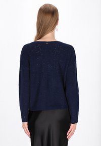 Pulover tricotat de culoare bleumarin, cu un model texturat, guler rotund și mâneci lungi. Prezintă accente fine de sclipici și un croi scurt.