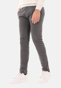 Pantaloni in cotone grigio con vestibilità slim, frontale piatto e tasche laterali, abbinati a scarpe da ginnastica bianche. Il materiale ha una finitura liscia e opaca.