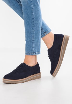 Granatowe zamszowe buty zapinane na sznurówki z niską podeszwą platformową, z ozdobnym przeszyciem i kontrastującą jasnobrązową podeszwą z gumy.