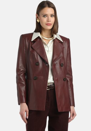 Maroon leather double-breasted jacket with large lapels, two buttons, and side pockets; paired with a white shirt and textured brown pants.