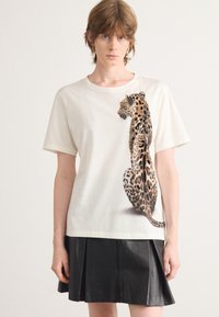 T-shirt en coton crème avec un graphique détaillé de léopard sur le devant. Le t-shirt a des manches courtes et une coupe décontractée.