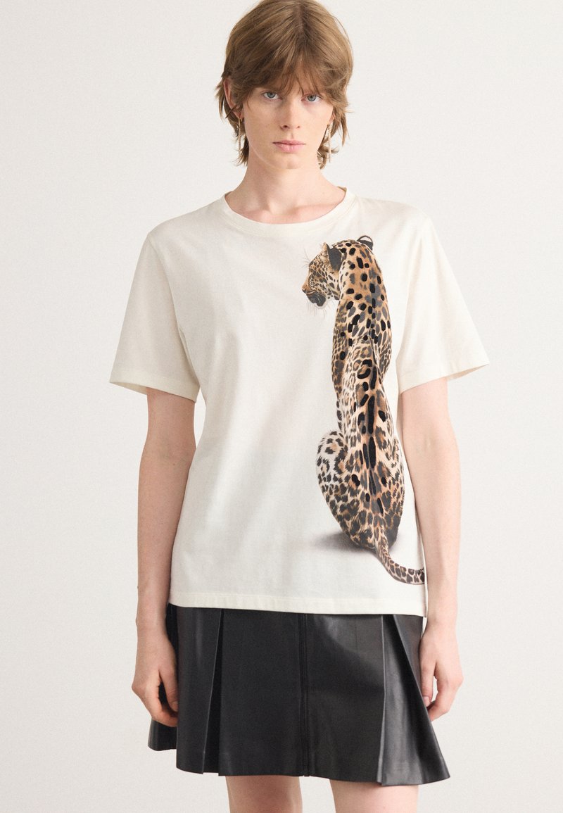 T-shirt en coton crème avec un graphique détaillé de léopard sur le devant. Le t-shirt a des manches courtes et une coupe décontractée.