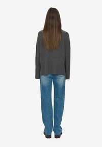 Sivkasta pletena jopica z ohlapnim krojem, v kombinaciji s svetlo modrimi širokimi hlačami. Model stoji z dolgimi lasmi vidnimi, obrnjen od kamer.