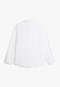 Chemise blanche à manches longues avec col boutonné, empiècement dans le dos et poignets à boutons ; tissu lisse avec une texture uni.