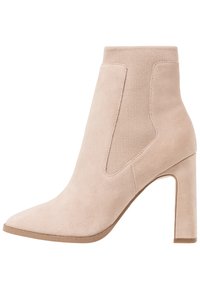 Bota beige de ante hasta el tobillo con puntera puntiaguda, paneles laterales elásticos y un tacón alto y grueso. Textura suave y diseño minimalista.