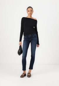 Top lungo nero con spalle scoperte abbinato a jeans skinny blu scuro. Accessoriato con una piccola borsa nera e ballerine con stampa animale.
