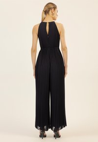 Jumpsuit noir long plissé avec un détail de dos en trou de serrure et une coupe évasée. Fabriqué dans un tissu doux, il présente une taille cintrée.