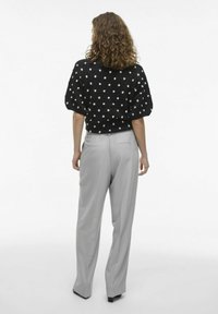 Pull noir à manches courtes avec des pois blancs, associé à un pantalon taille haute gris clair, avec une coupe décontractée et une texture lisse.