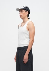 Balts plāns krekls bez piedurknēm, valkāts kopā ar tumšām biksēm. Melna un balta cepure. Vienkāršs dizains bez rakstiem. Tīras līnijas, minimālistiska tekstūra.